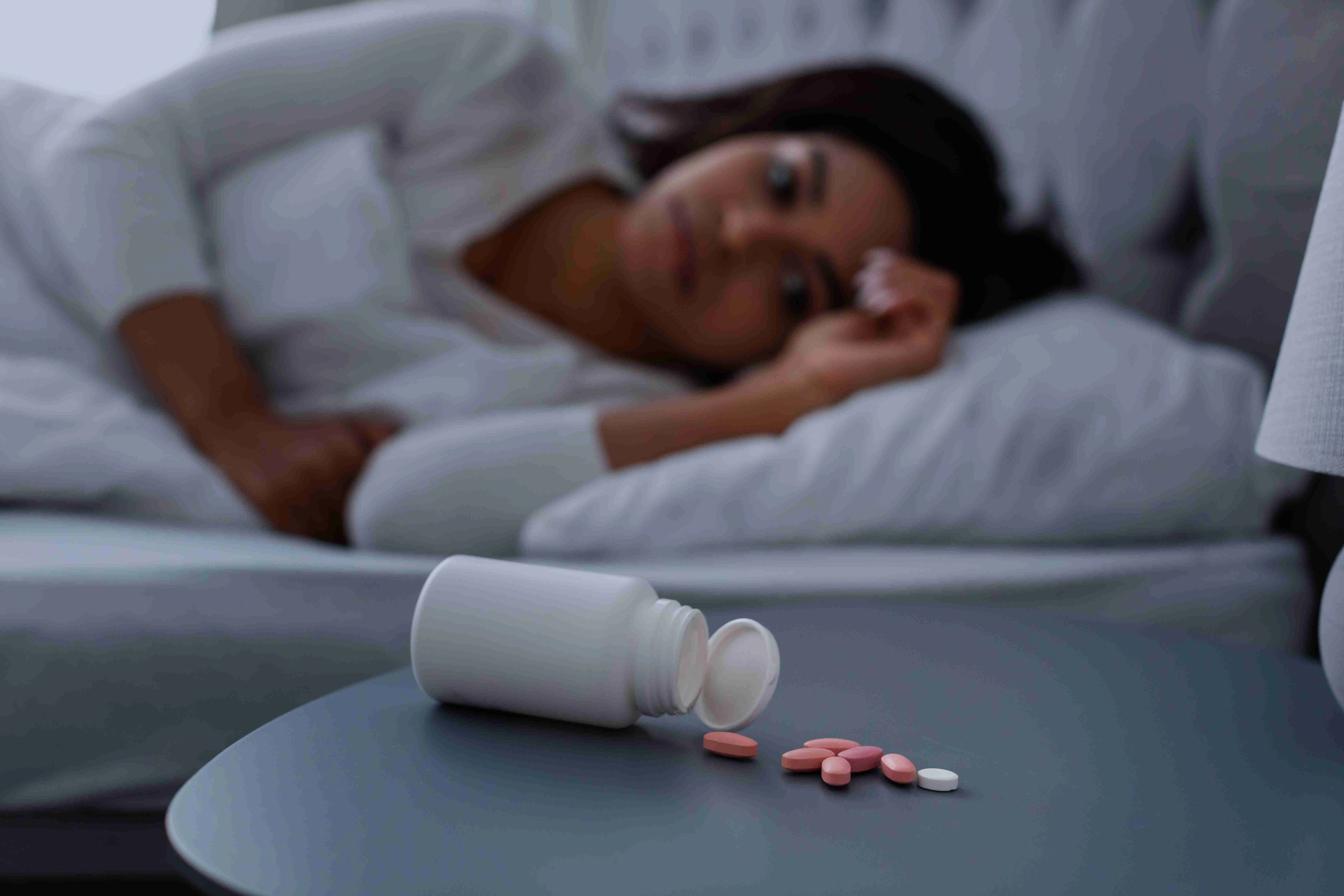 Black woman suffering from insomnia, pills lying on table