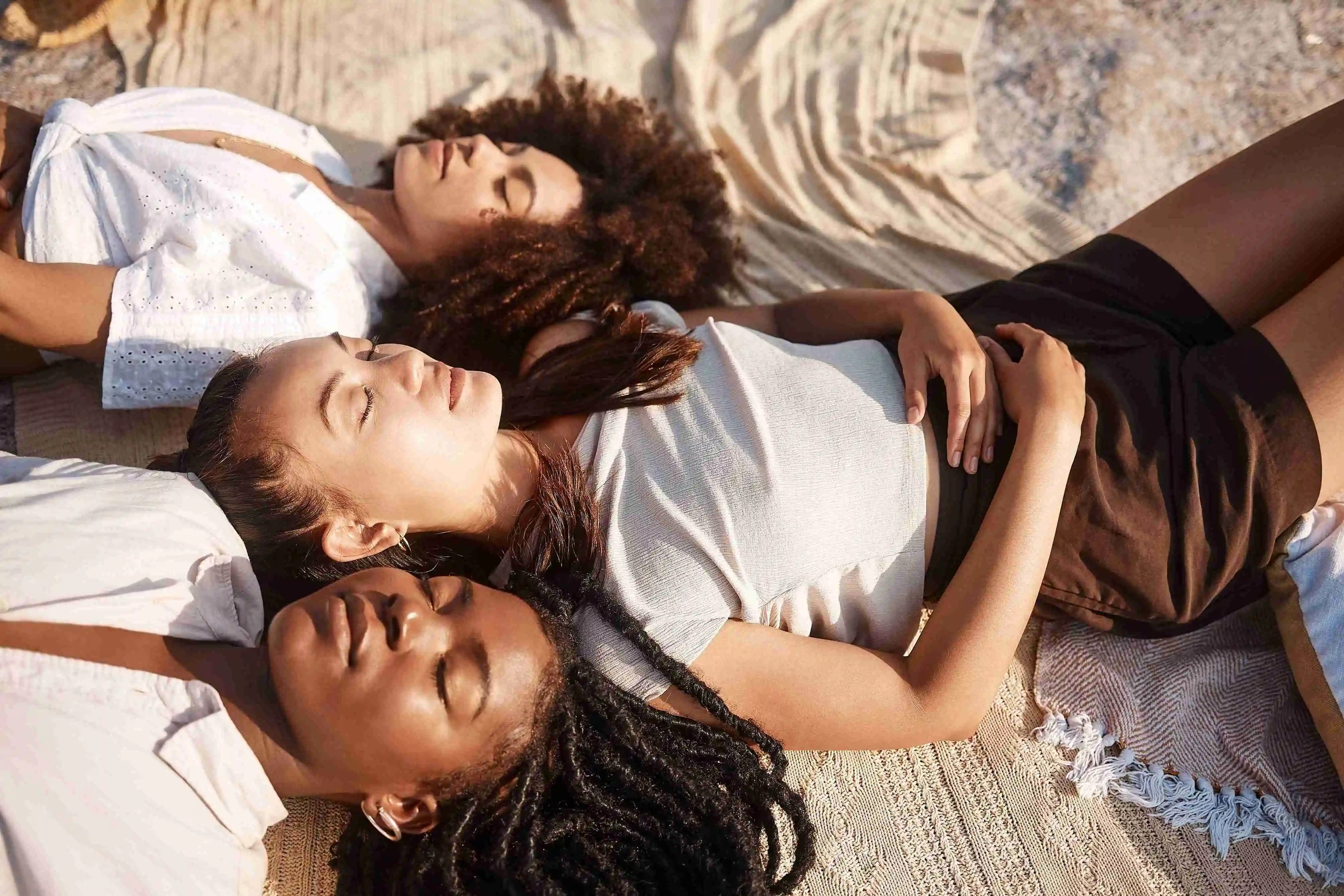 Young diverse female friends laying on the beach together resting with their eyes closed