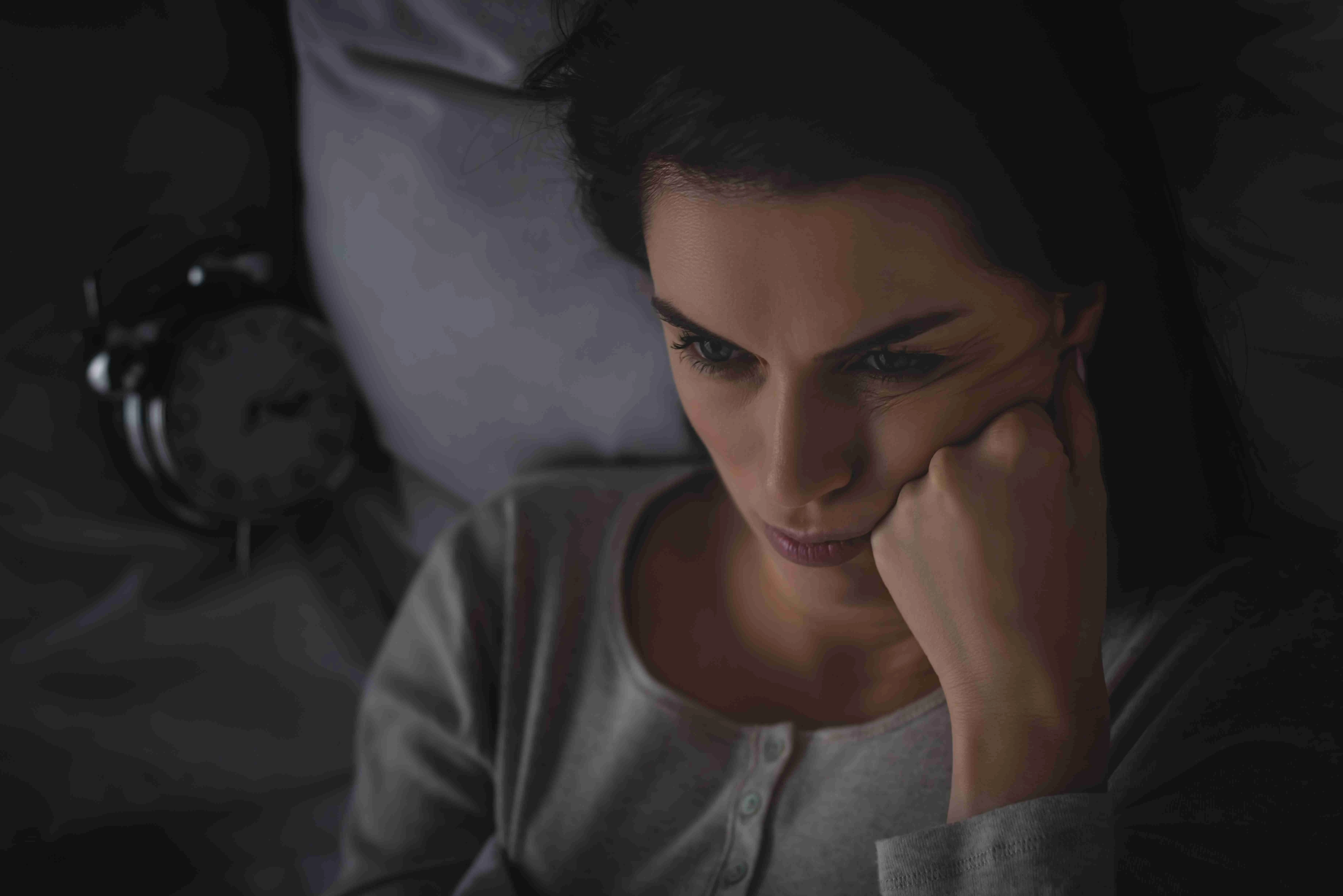 top view of upset woman with insomnia lying on bed near alarm clock