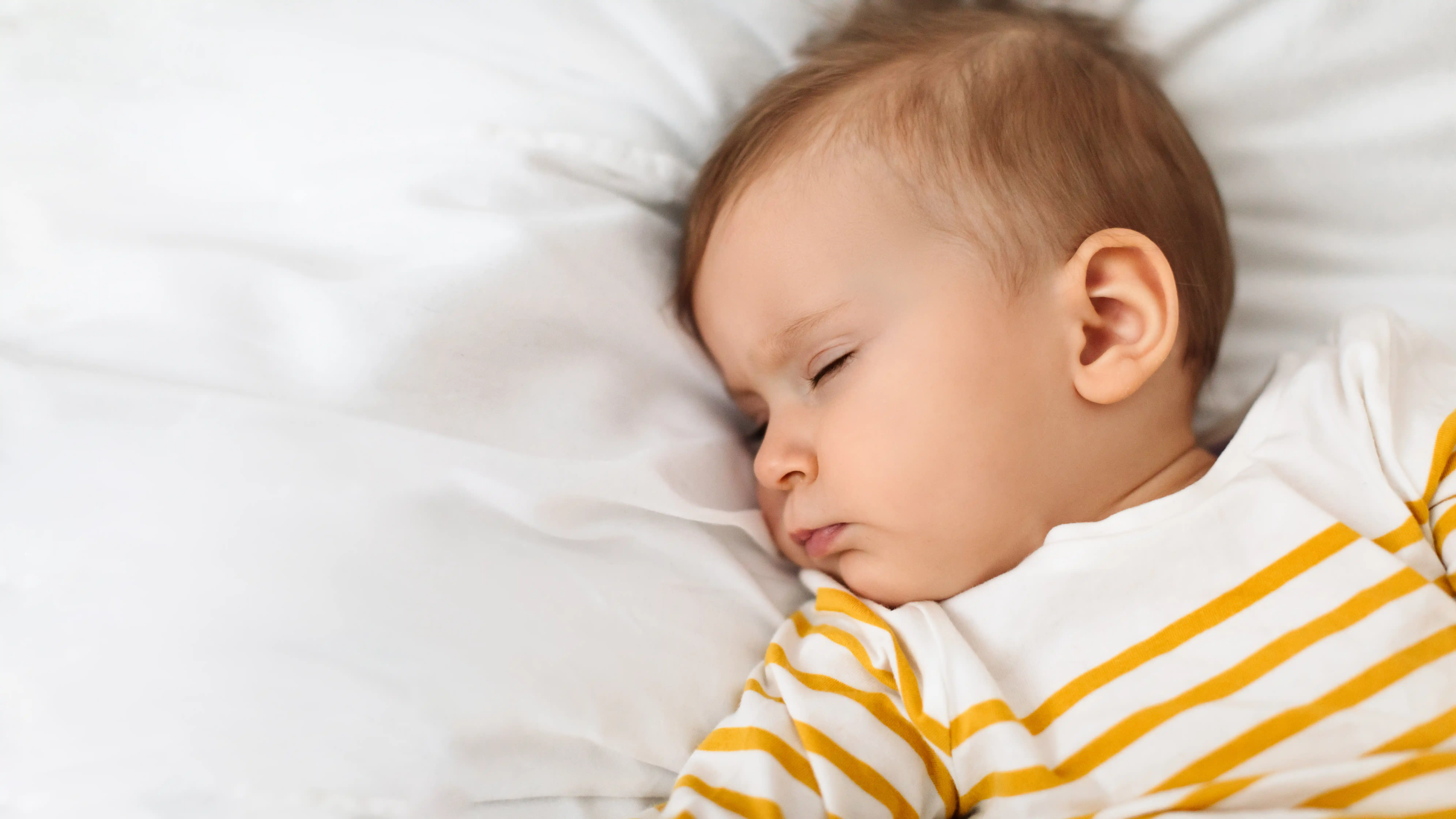 Beautiful baby girl sleeping peacefully on bed, resting during daytime sleep with eyes closed