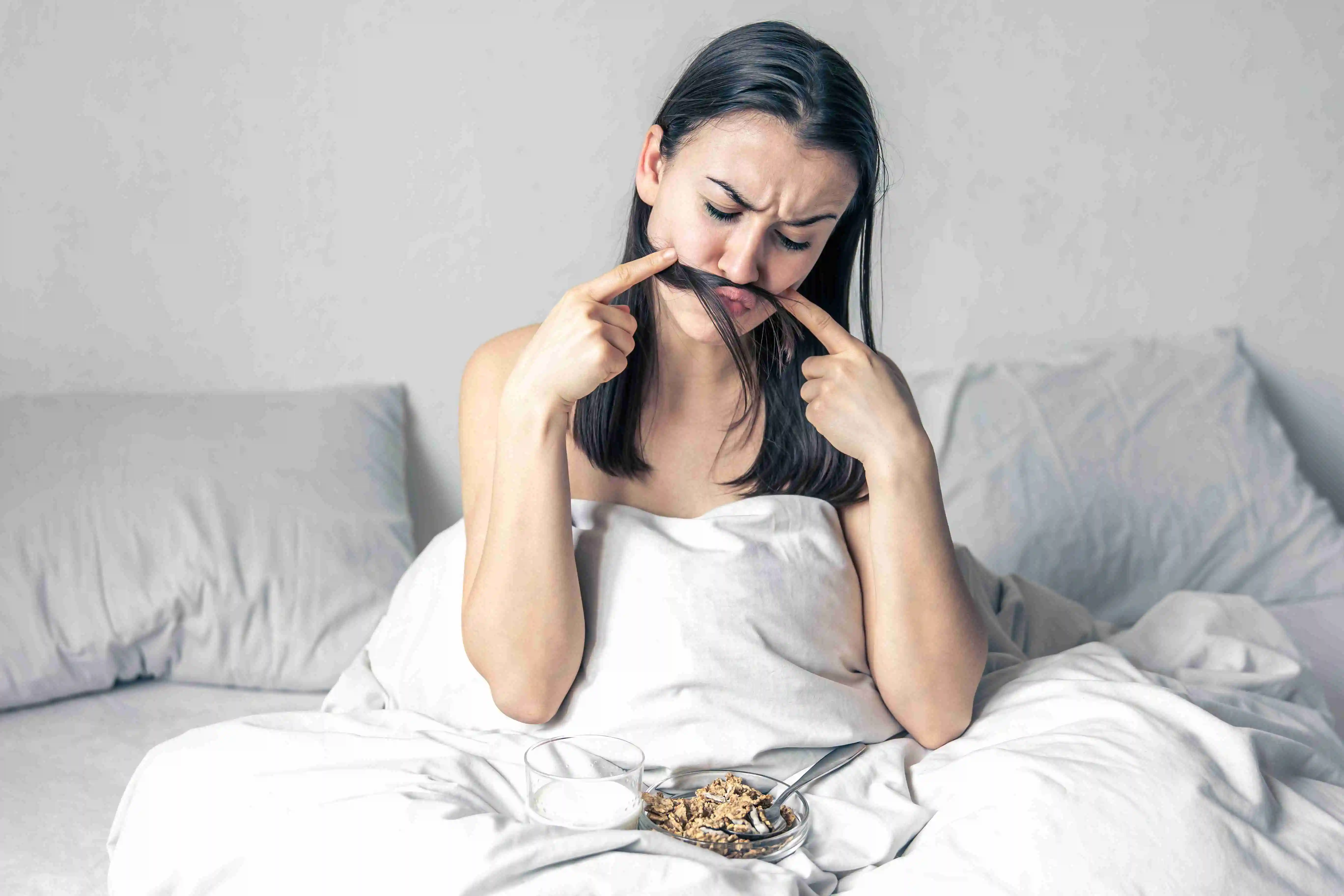 A young woman in white bed with cereal and milk.