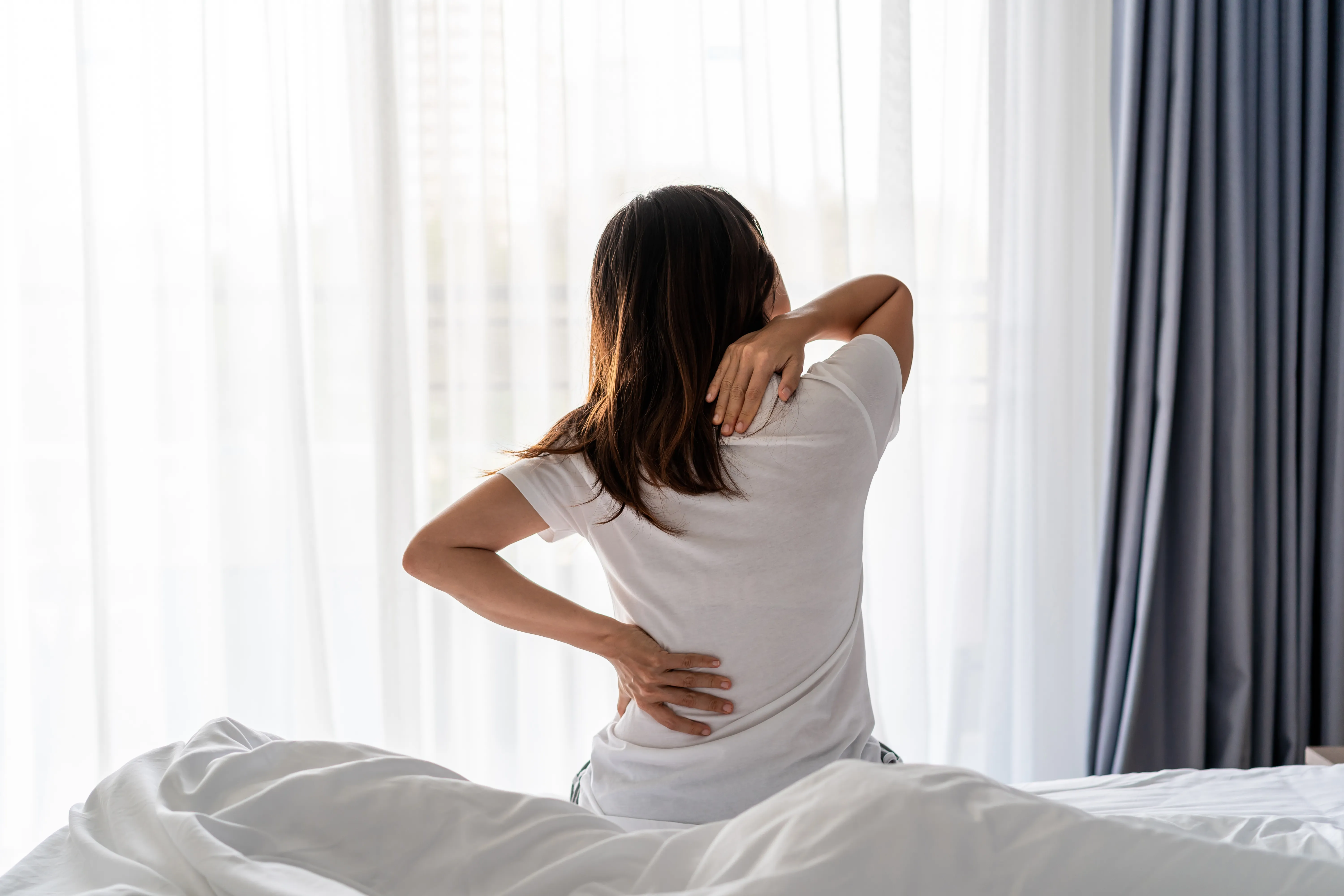 Woman suffering from back ache and neck ache on the bed, health care and problem concept