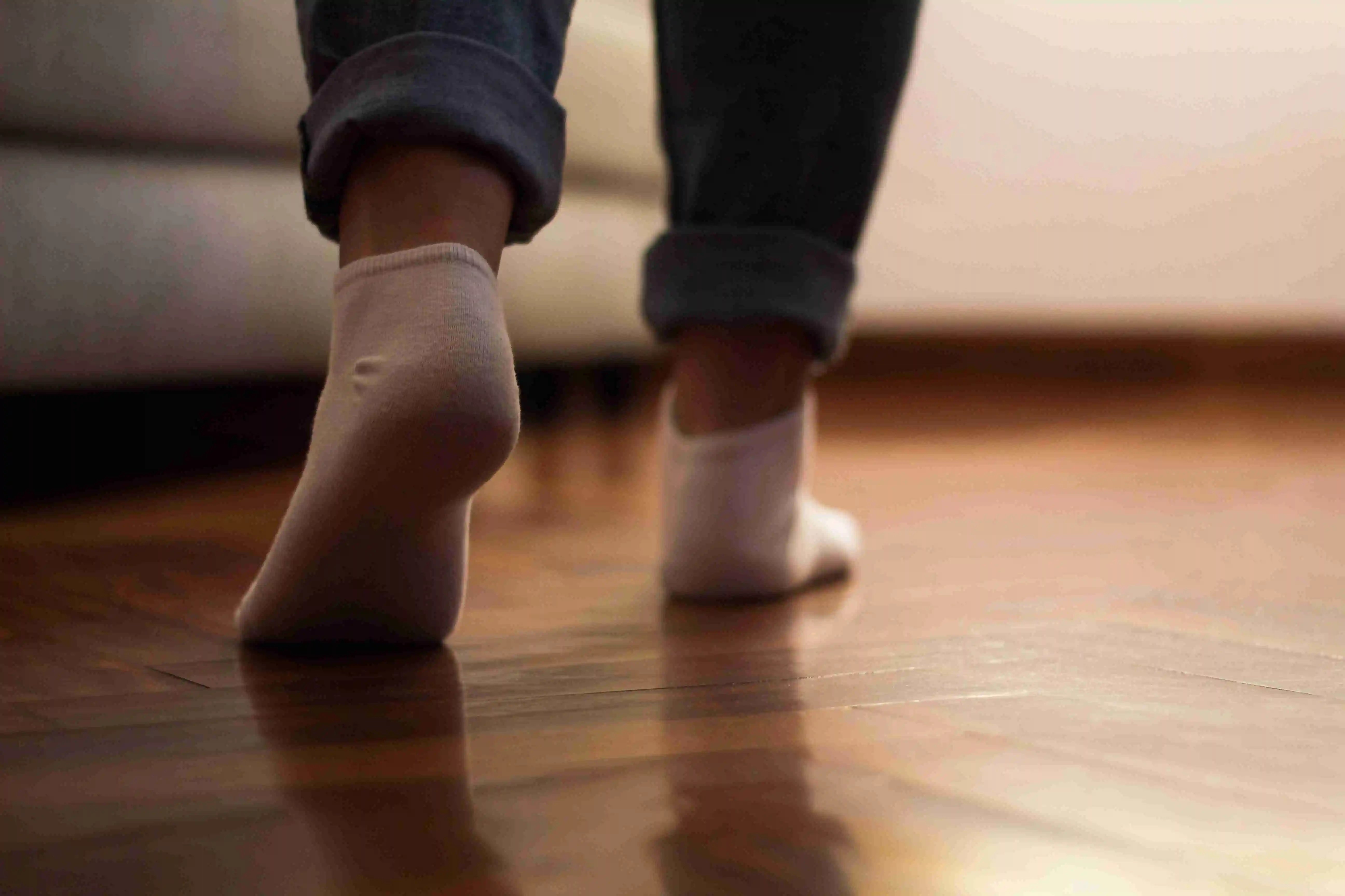 Legs of a unrecognizable woman in jeans and socks walking on the wooden floor