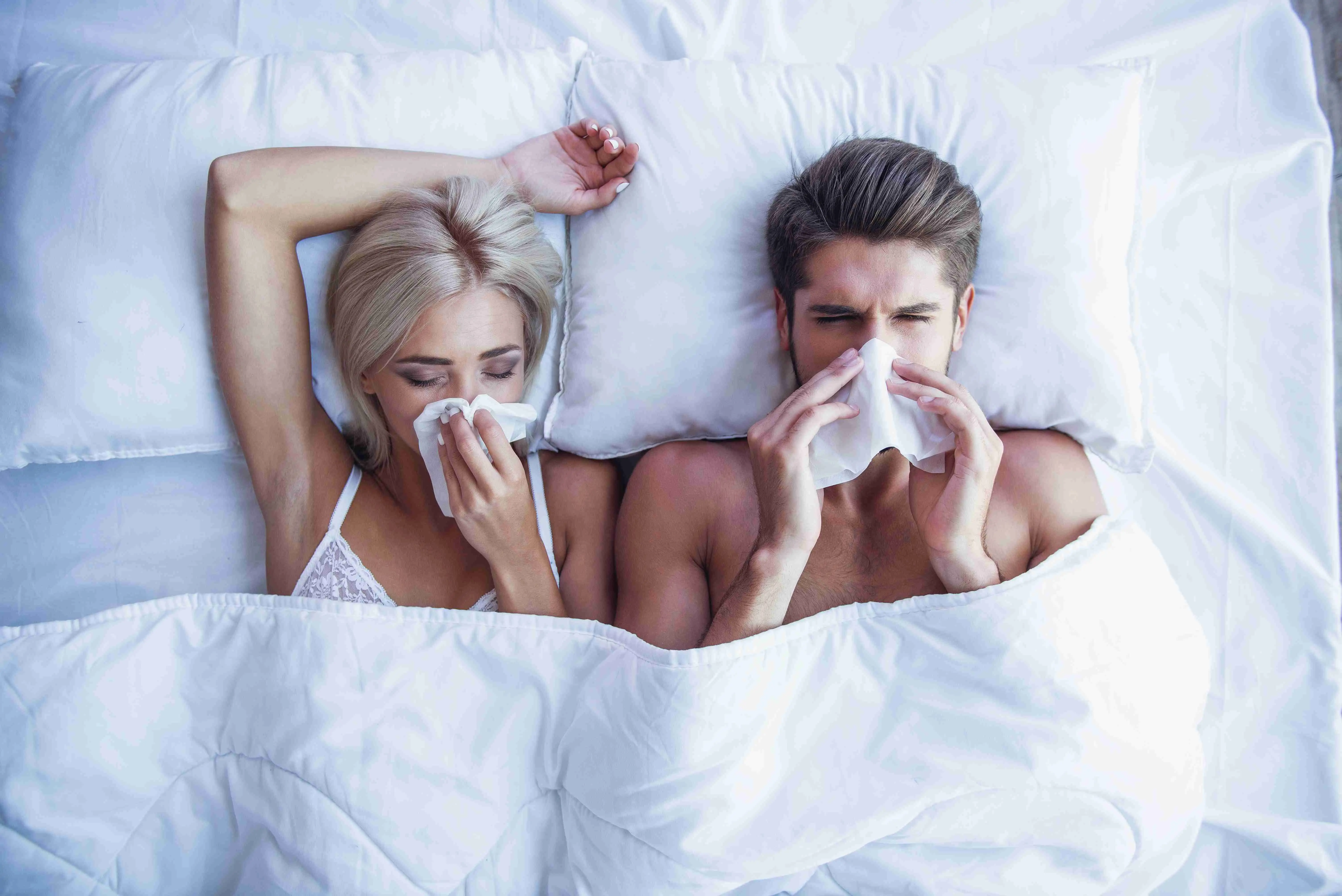 Top view of beautiful young couple wiping noses while lying in bed