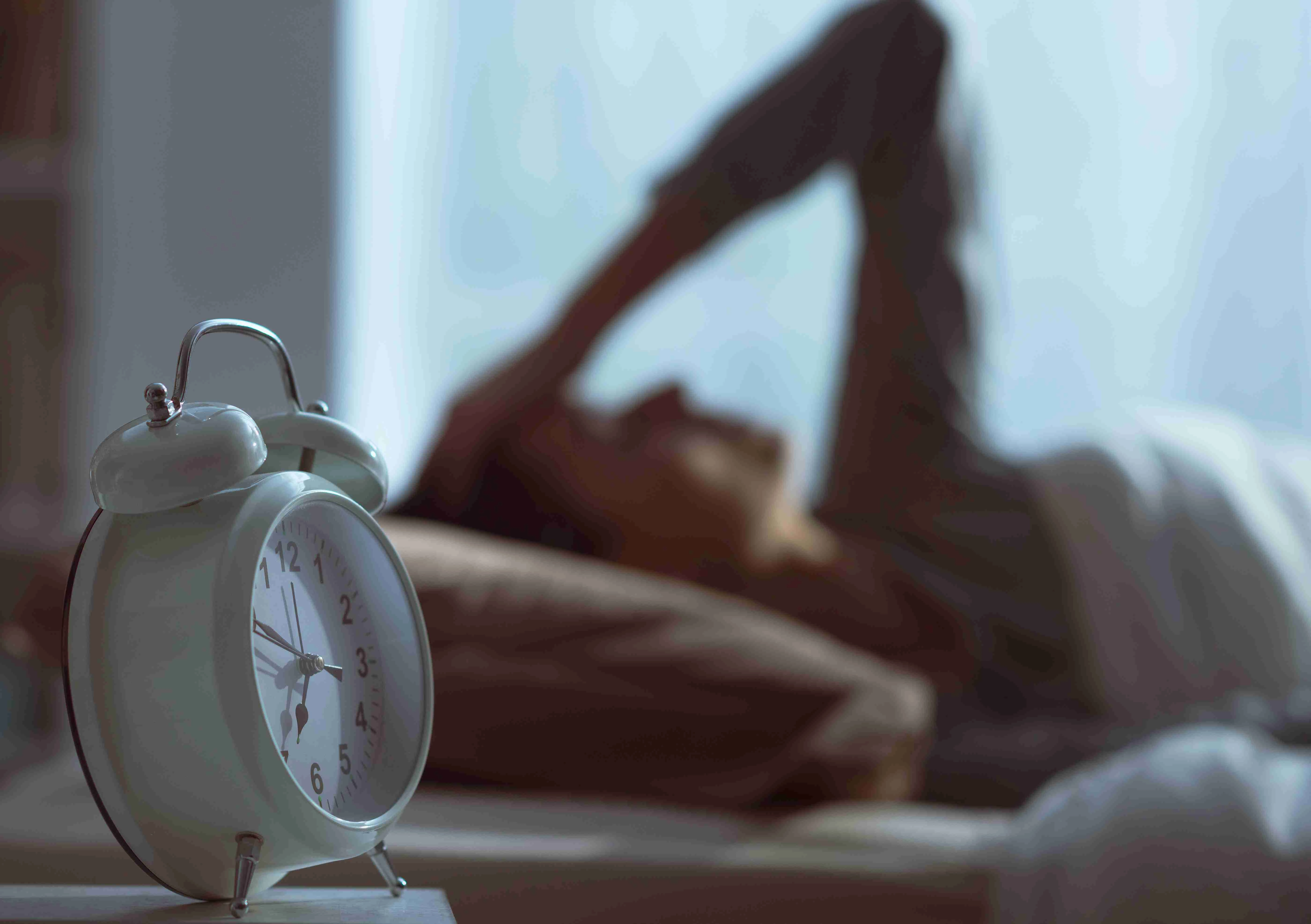 Woman waking up in the morning and alarm clock in the foreground