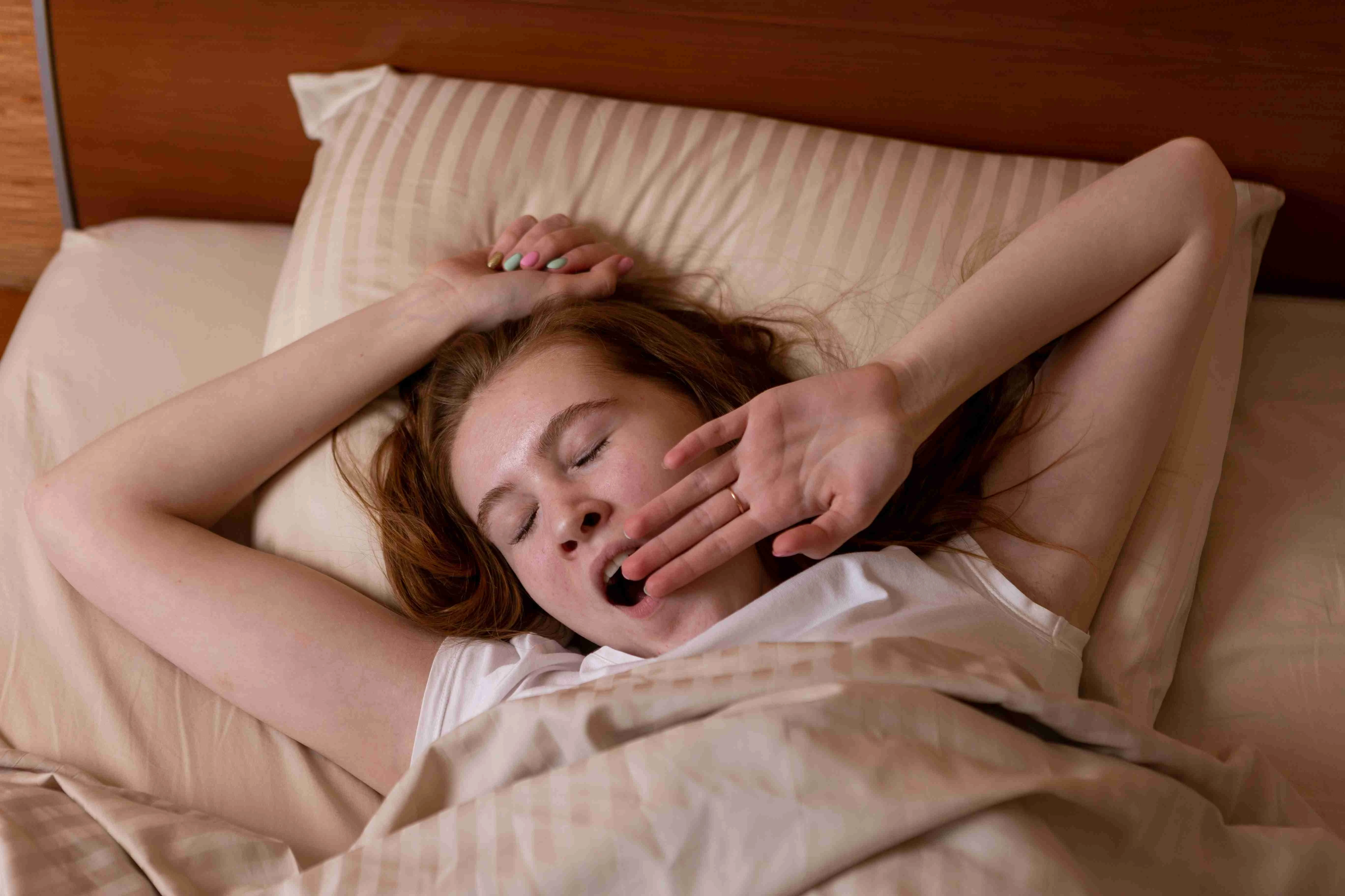 Young teen girl lies on the bed and yawns