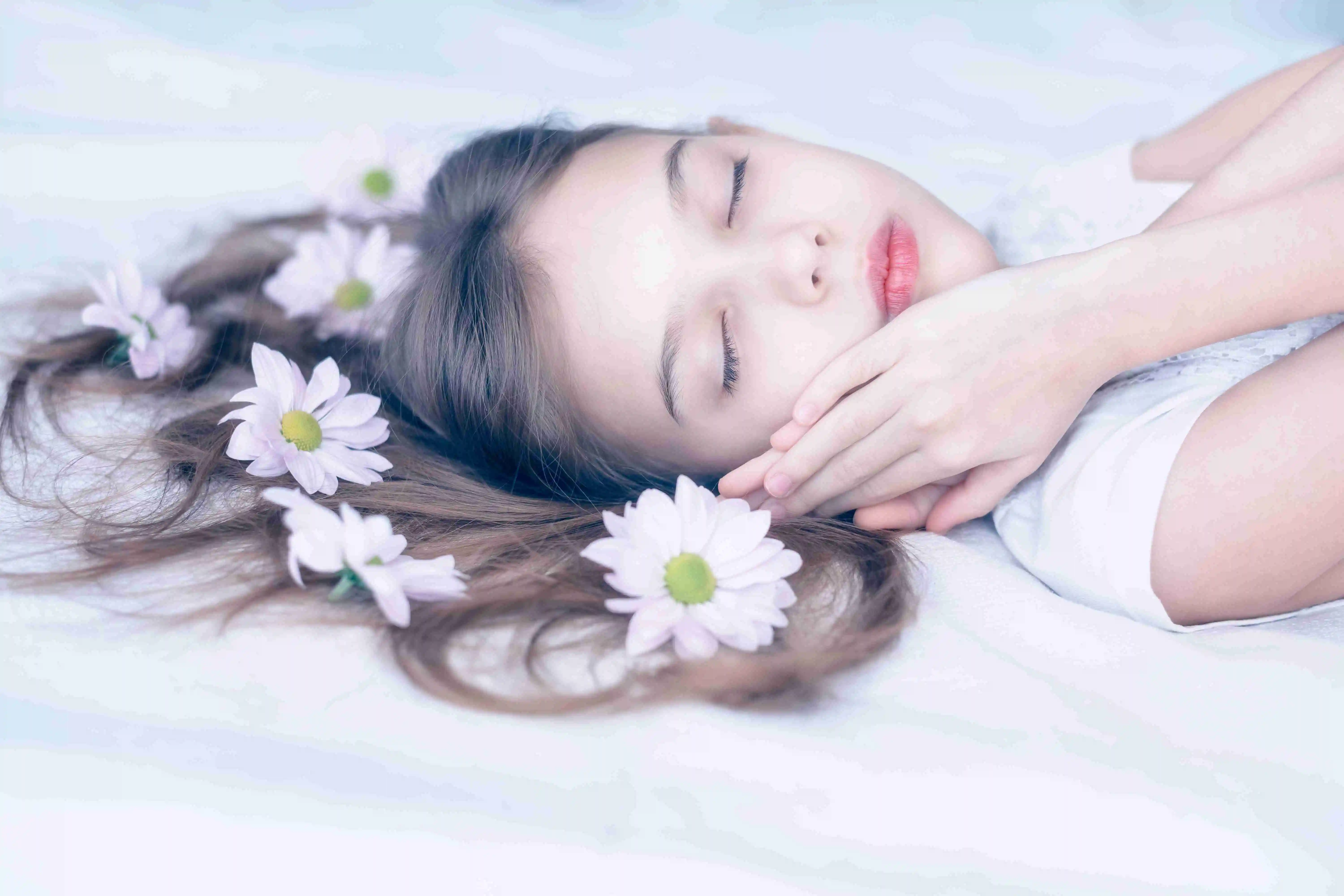 beautiful Caucasian girl sleeping with daisy flowers in her long hair on white.