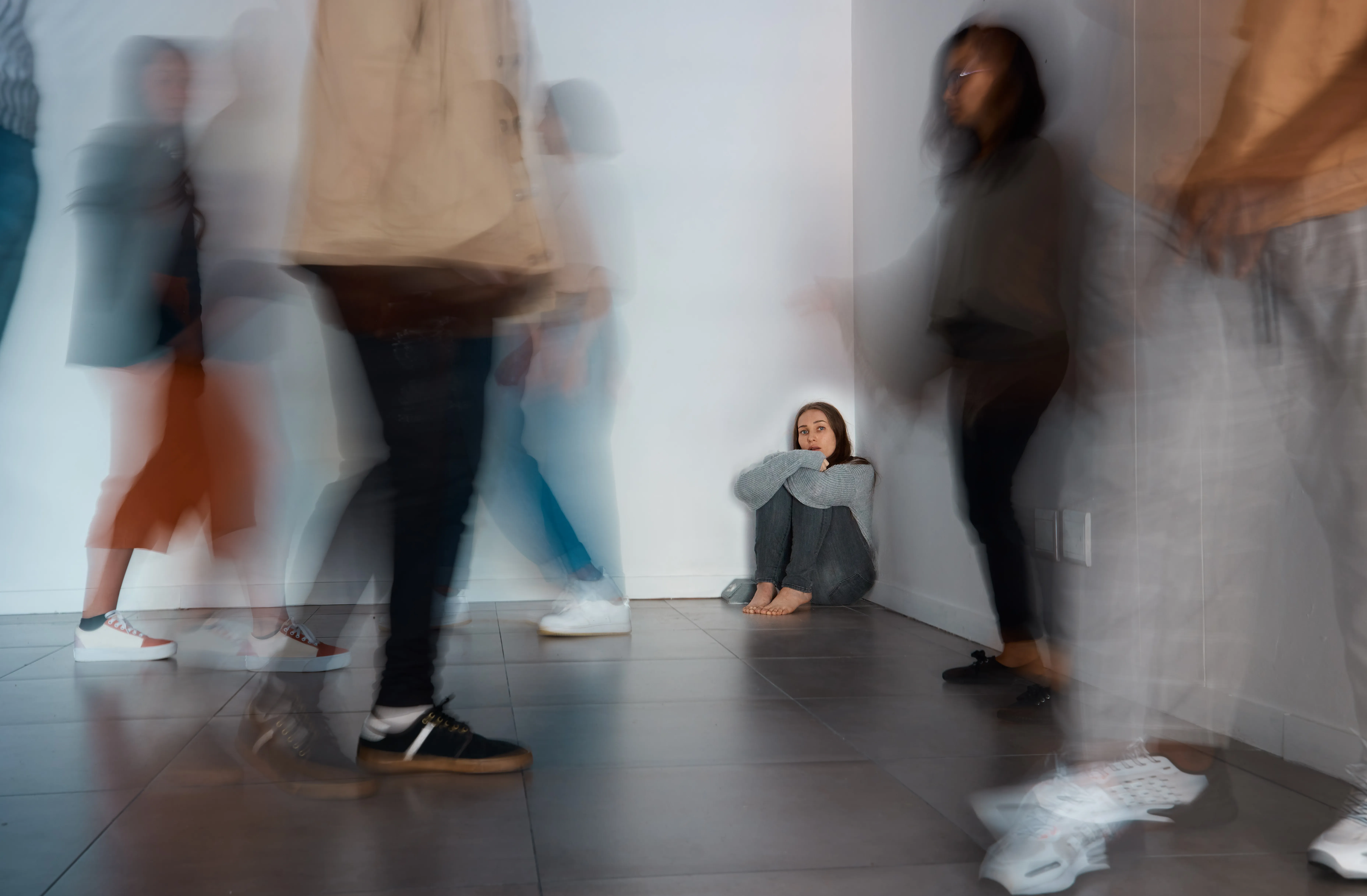 Shot of a young woman sitting on the floor with people around her.