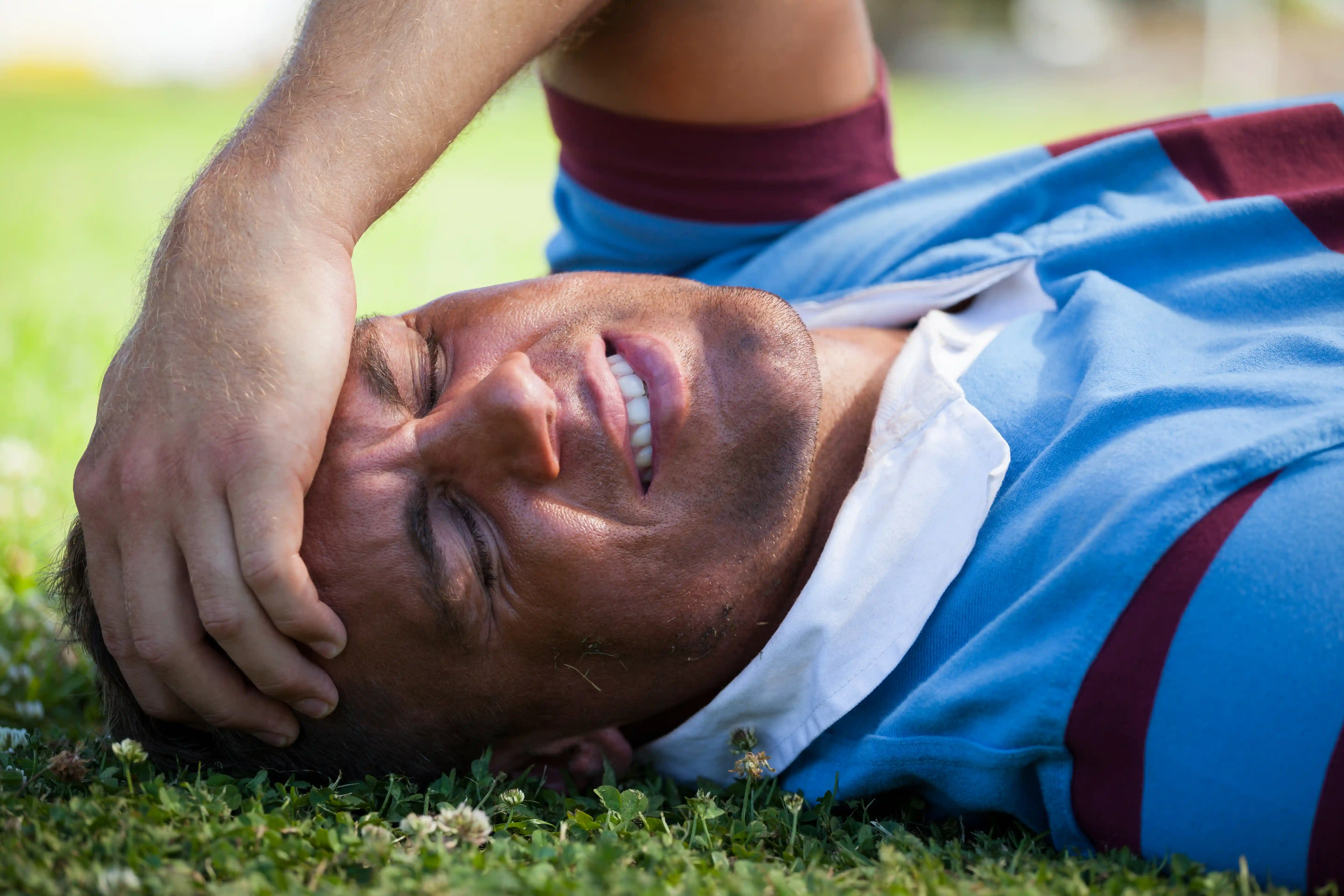 Injured rugby player with eyes closed lying on playing field