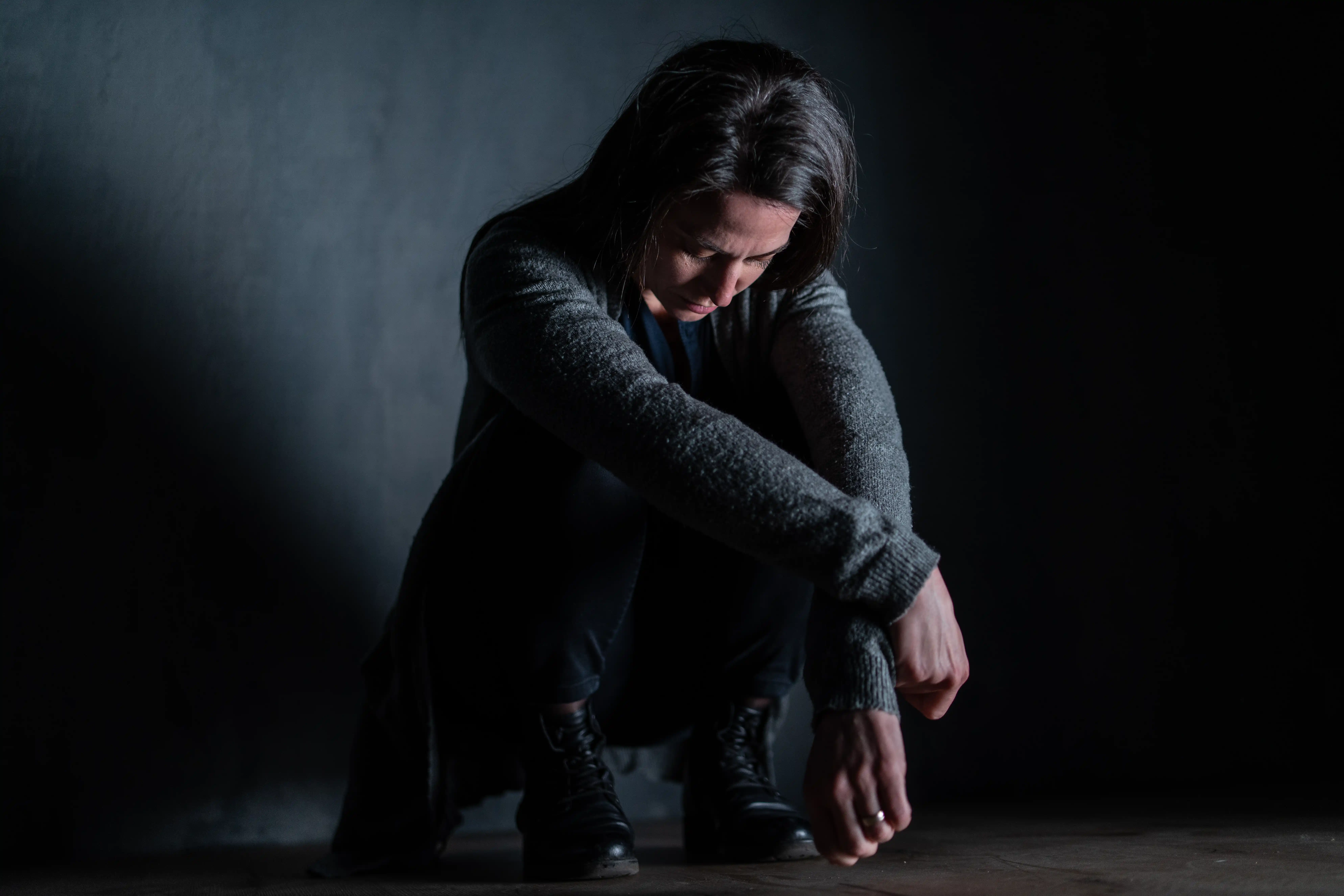 Sad mid-adult woman, alone in darkness, sitting and thinking