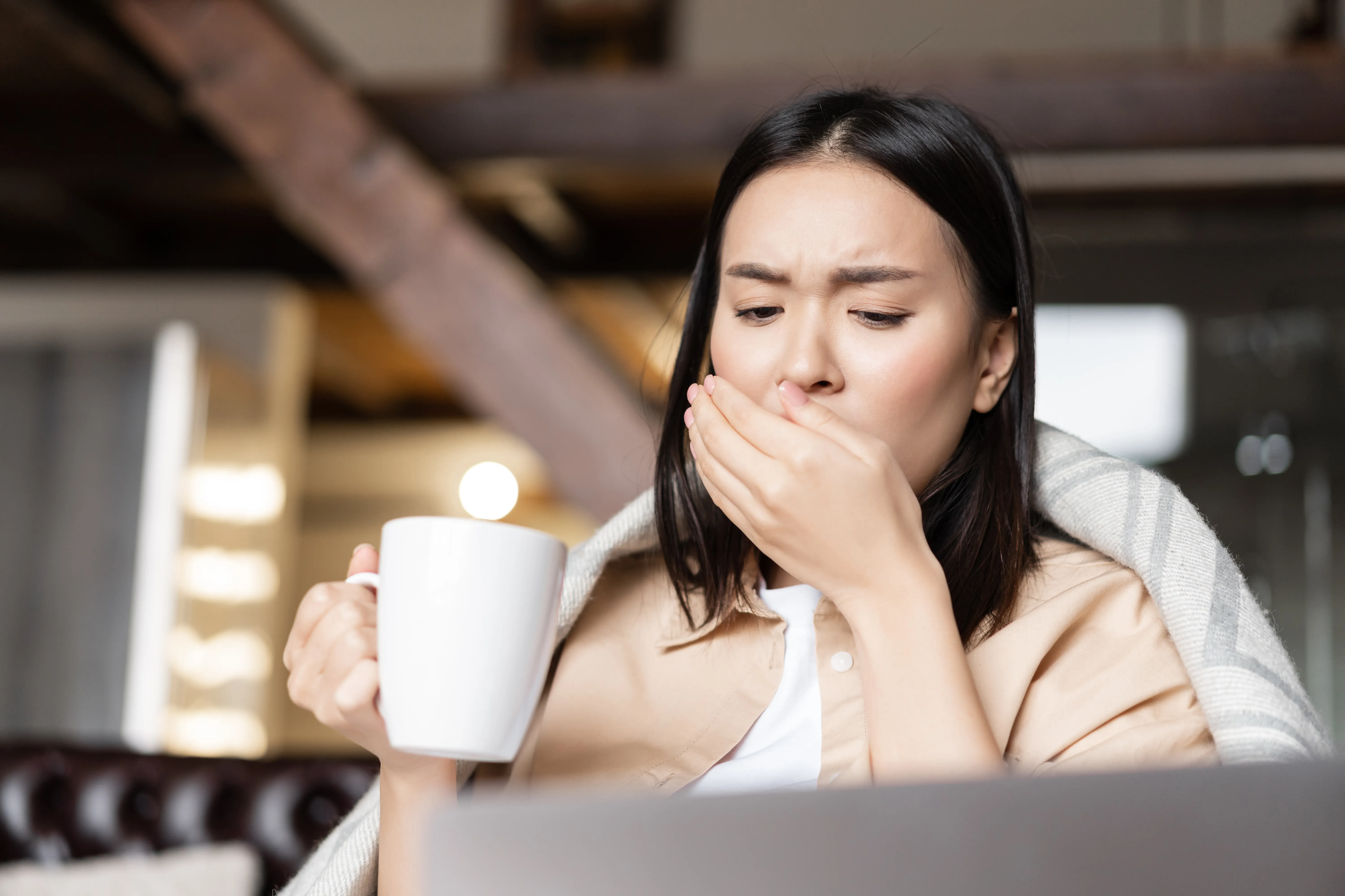 Portrait of sick asian woman at home, coughing and drinking hot tea, catching flu or covid-19