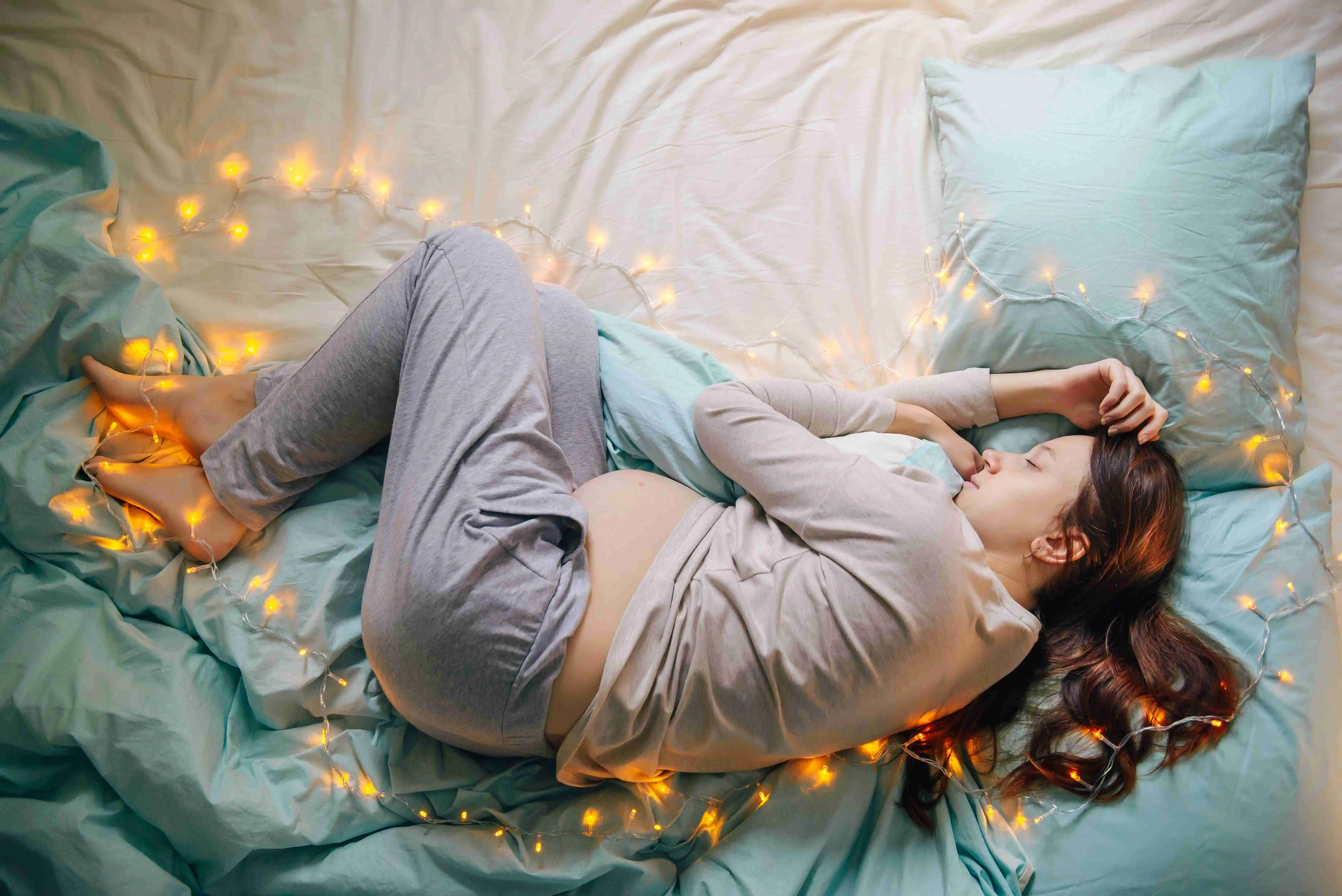 Young caucasian woman expecting baby sleeping on a bed decorated with lights,expressing upcoming fest and miracle of life