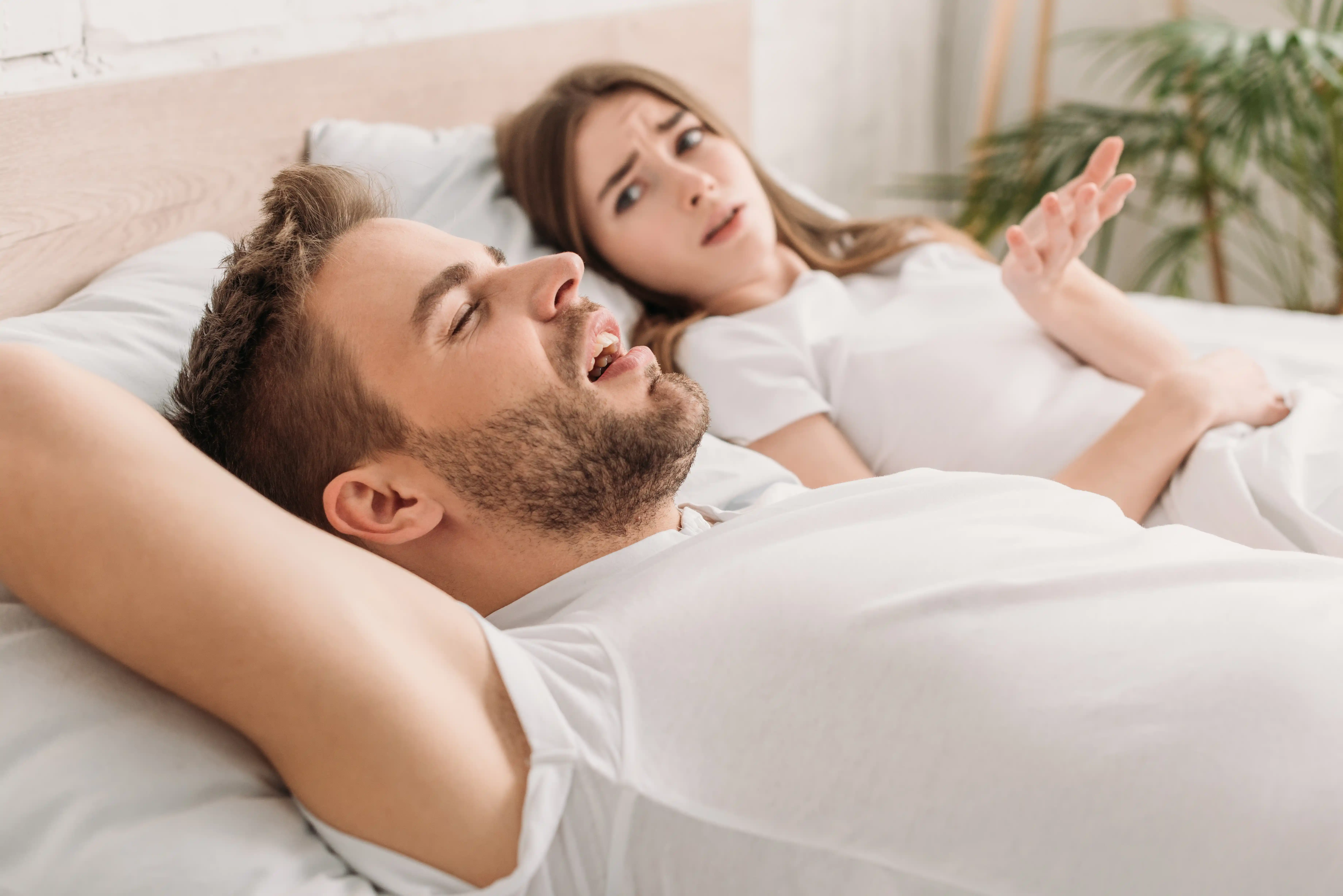 dissatisfied woman showing outrage gesture while lying in bed near snoring husband