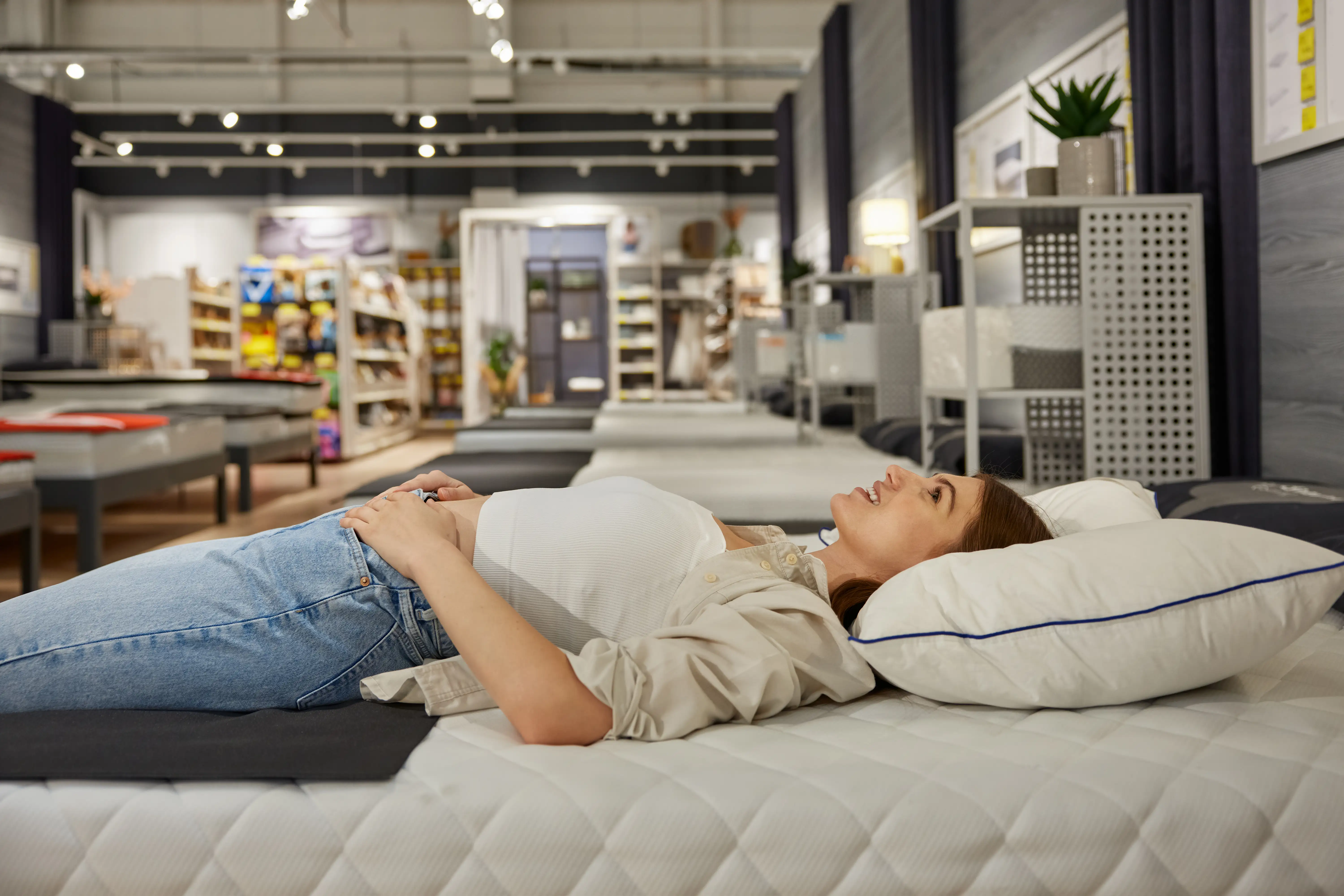 Young woman shopper choosing new bed at modern furniture showroom