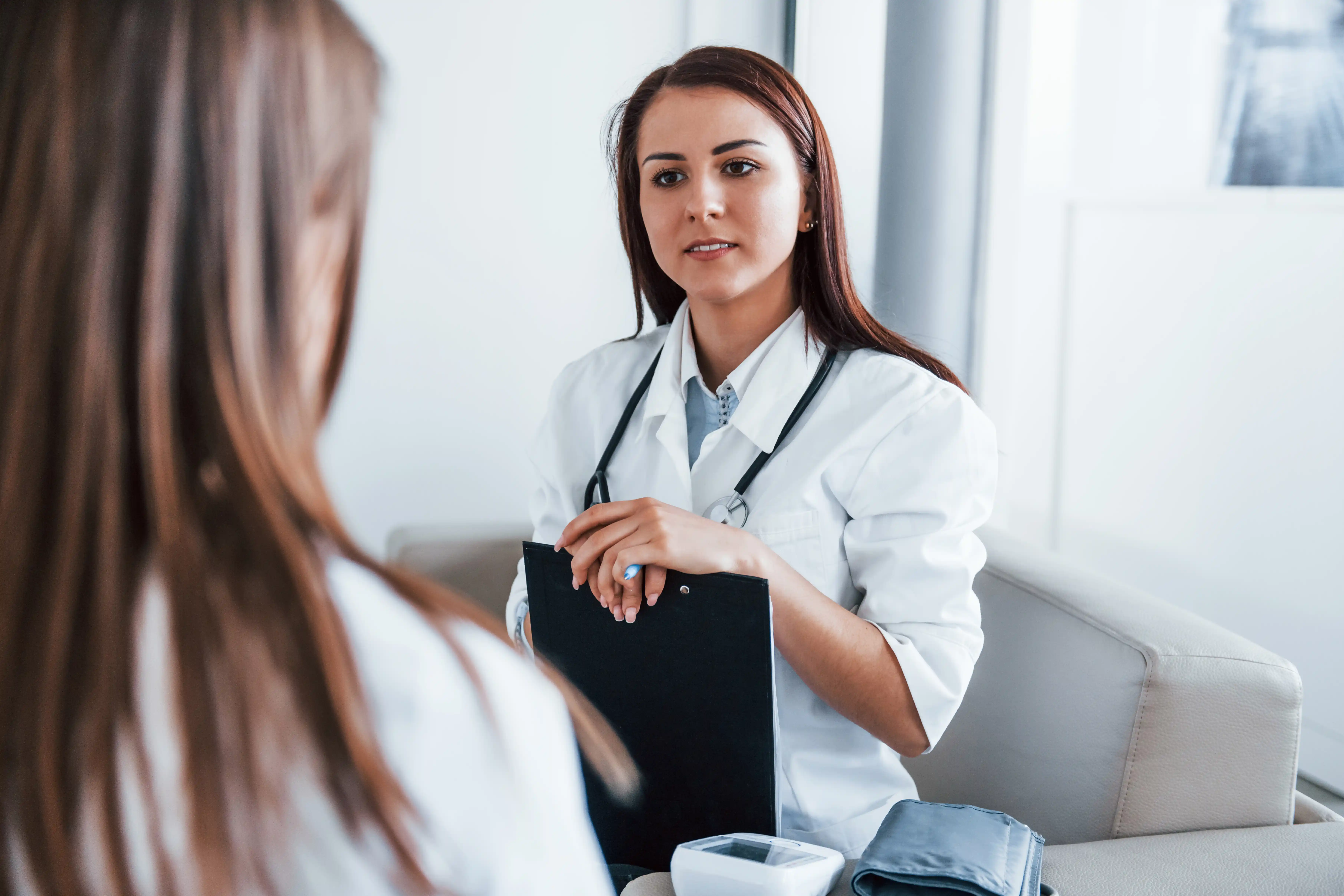 Sitting and talking. Young woman have a visit with female doctor in modern clinic.