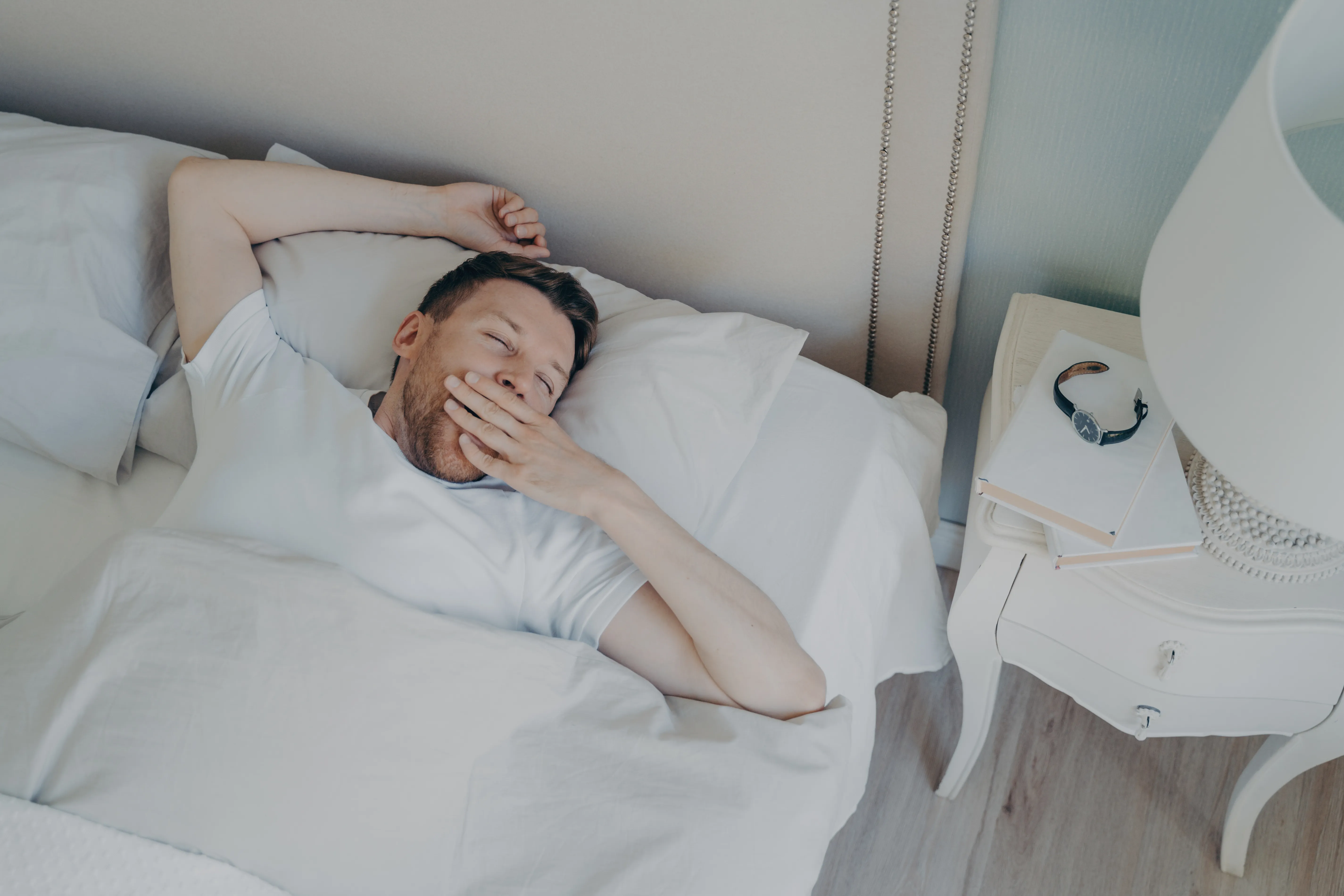 Cheerful young attractive man waking up in morning in bed