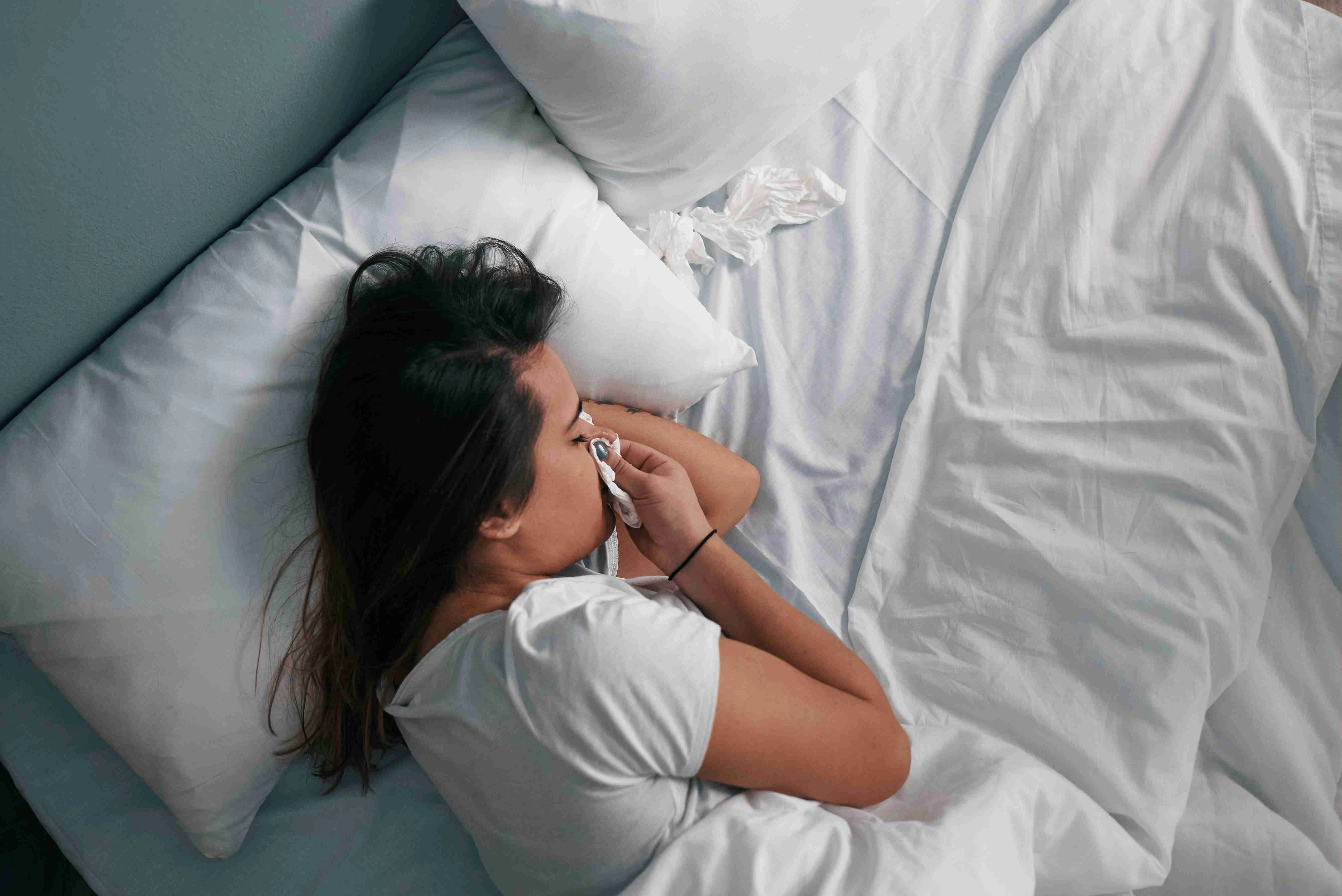 Close-up of a young Latin girl blowing her nose with a tissue while in bed