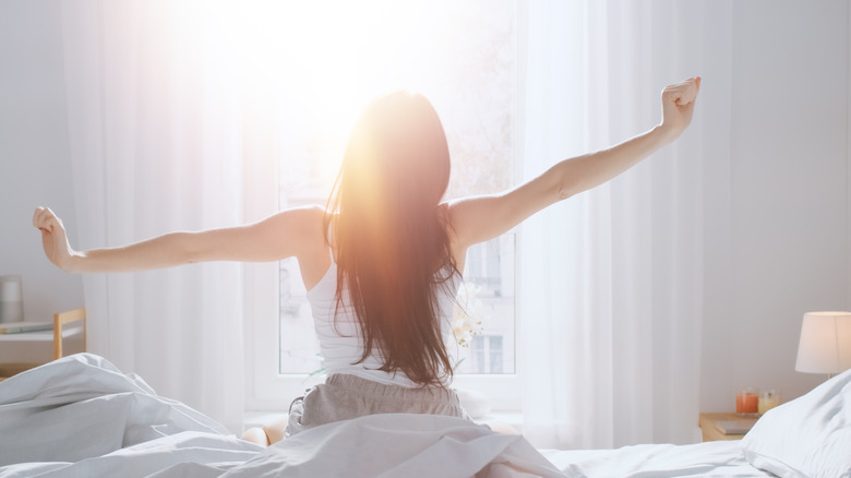 woman waking up in bed while sunshine coming through window