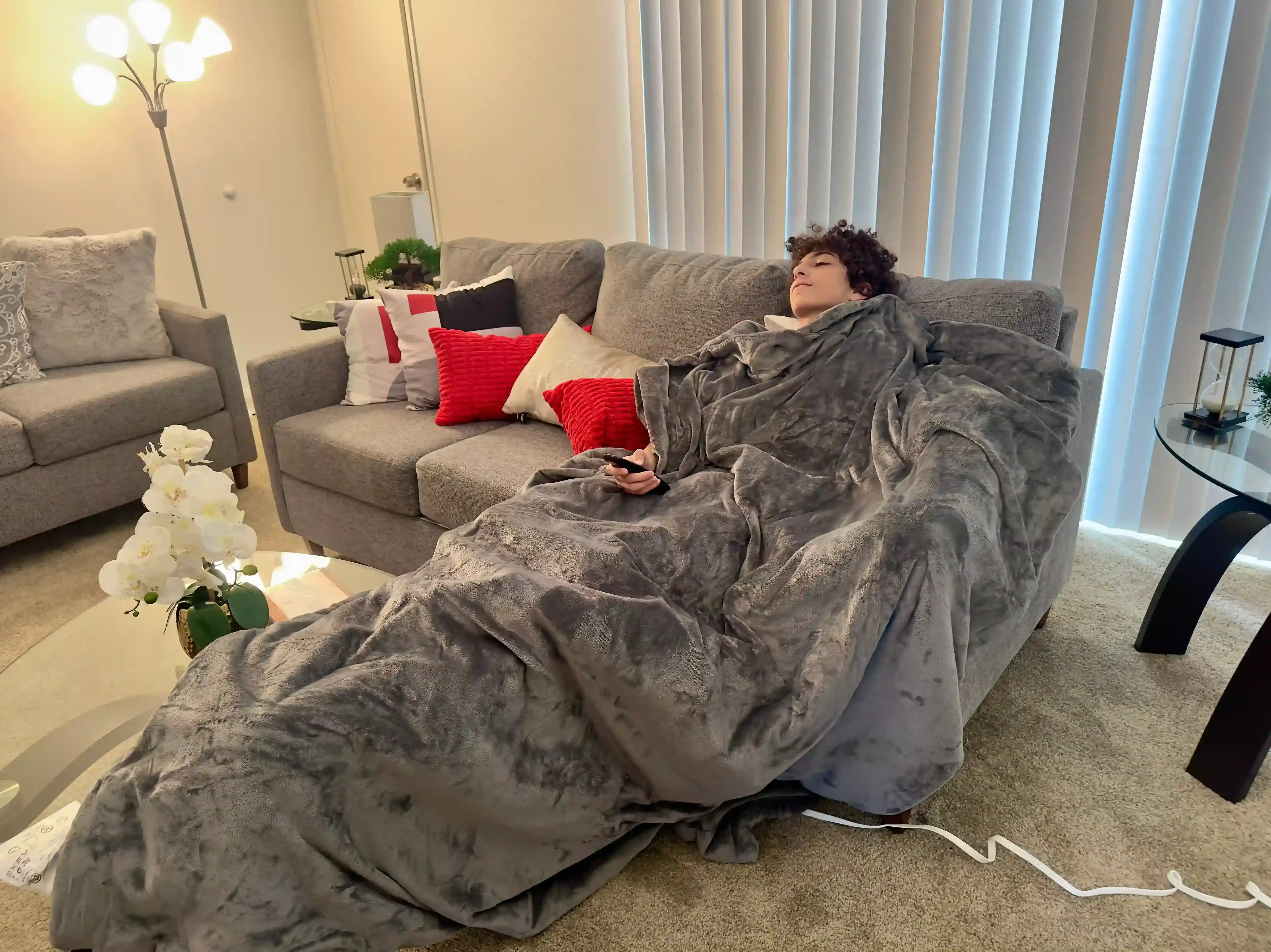 A reviewer from Sleepiverse Studio sitting on a couch, comfortably wrapped in a Zonli Heated Weighted blanket.
